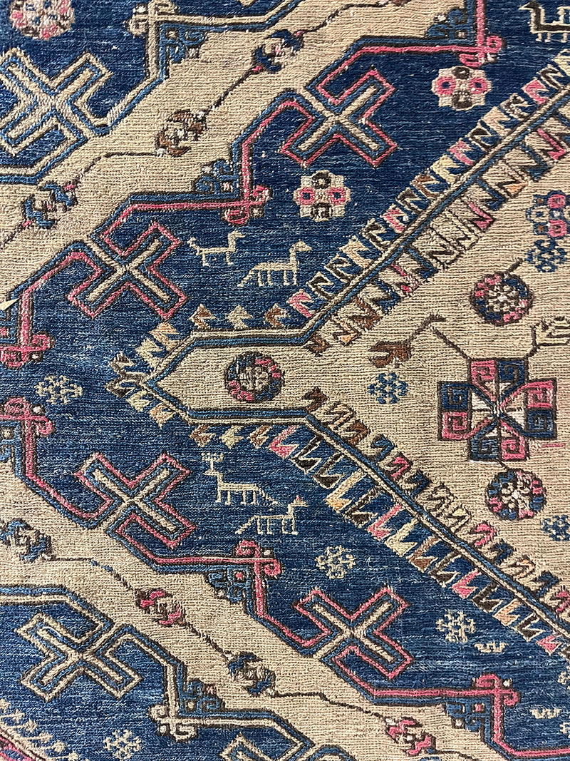a large antique sumac rug with pink and royal blue accents on a taupe field