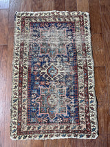 a mini antique heriz karajah rug with a dark blue field and green, pink and rust accents