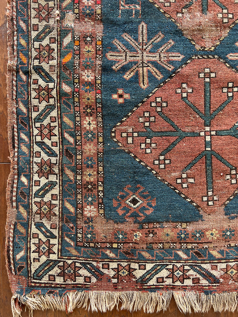 an antique caucasian rug with a dark prussian blue field and three coral-toned medallions