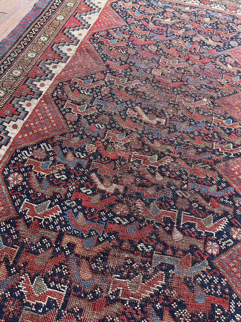 an antique qashqai rug with a dark blue field and bird pattern