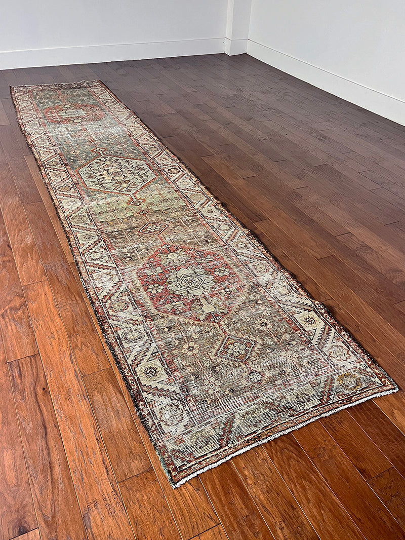 an antique kurdish runner with a grey green field, dark red and icy blue accents and a cream floral pattern