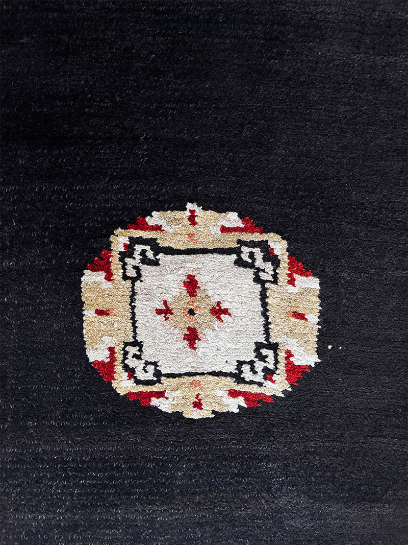 a small tibetan rug with a black field and a pretty red and yellow geometric design