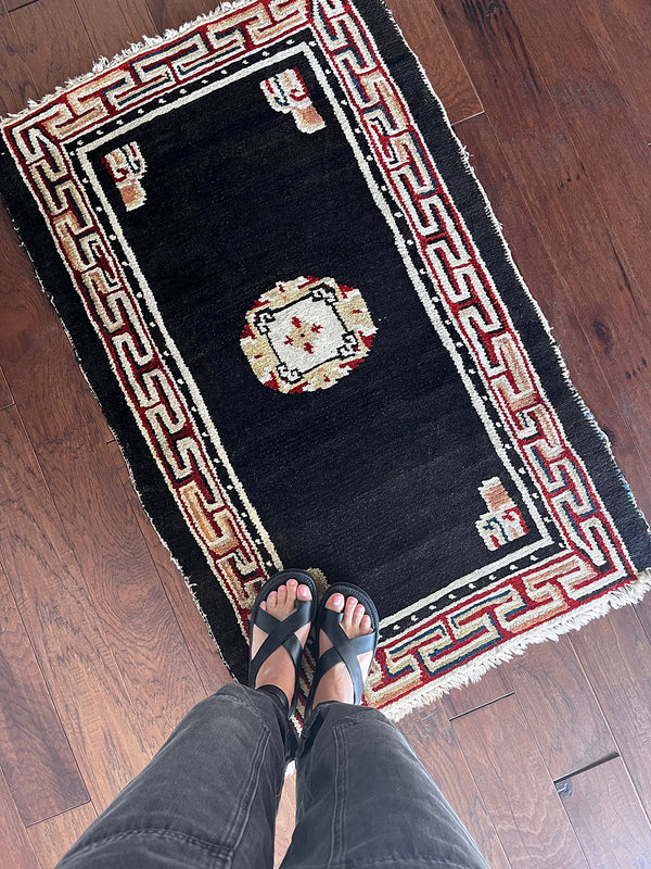 a small tibetan rug with a black field and a pretty red and yellow geometric design