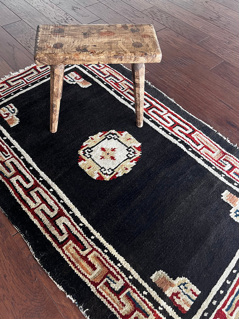 a small tibetan rug with a black field and a pretty red and yellow geometric design