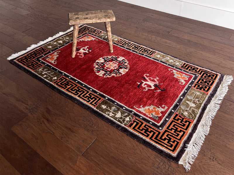 a vintage tibetan meditation rug with a solid raspberry red field and a pretty lilac and sage border in a geometric and floral design