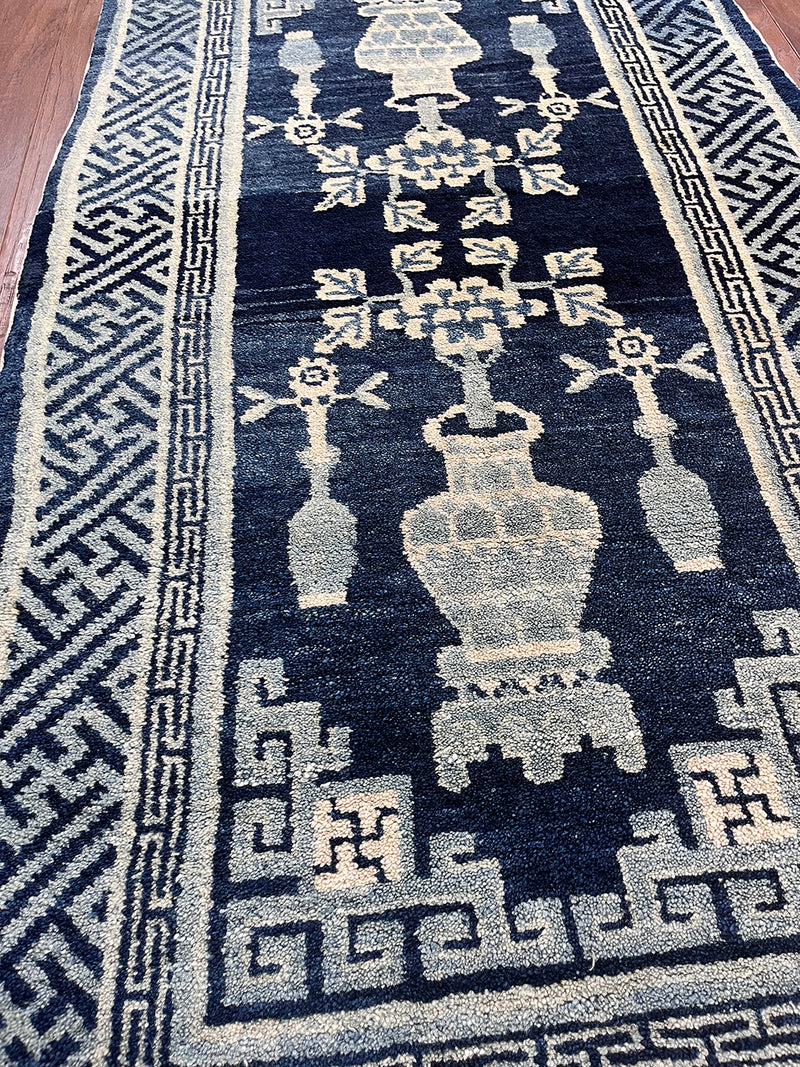 an antique chinese peking rug with a solid blue field and traditional chinese jar design in light blue and cream