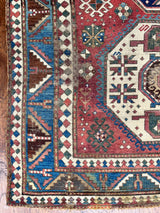 an antique kazak rug with a raspberry field and a geometric pattern in cream and prussian blue
