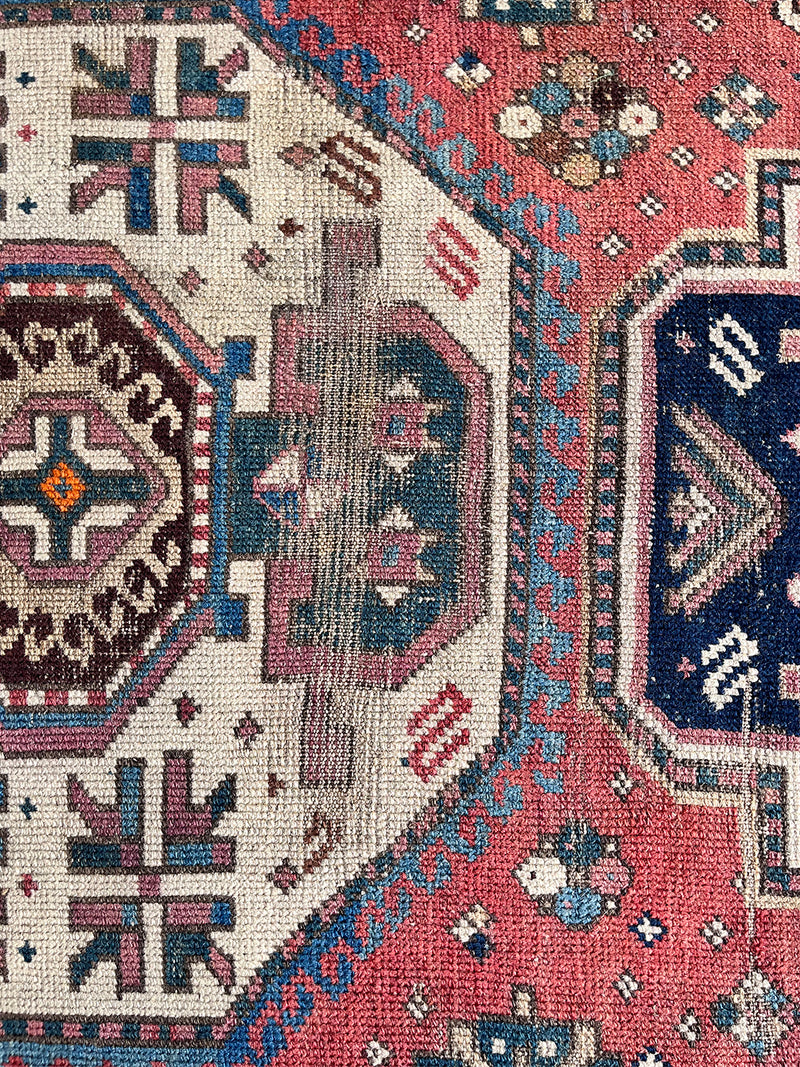 an antique kazak rug with a raspberry field and a geometric pattern in cream and prussian blue