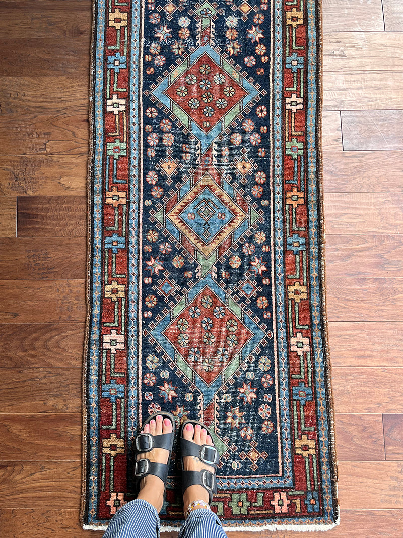 an antique mini heriz runner with a dark blue field, green accents and brick red medallions