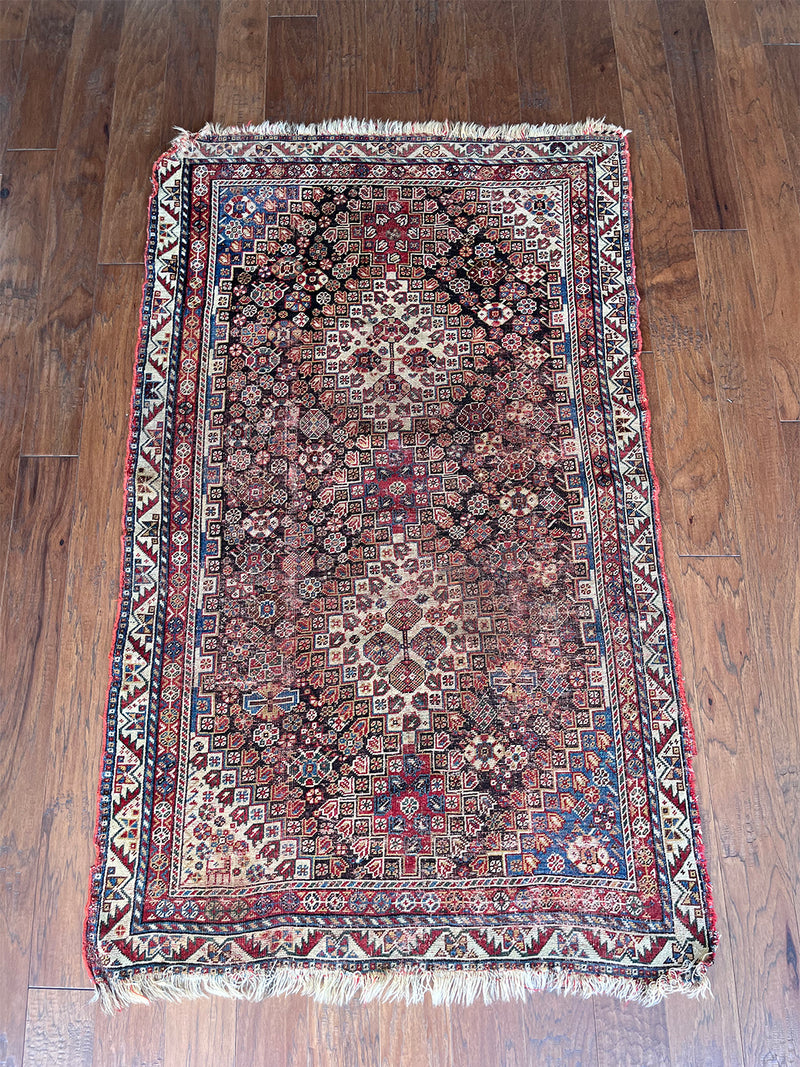 an antique shiraz rug with rust, brown and blue hues with an intricate floral pattern