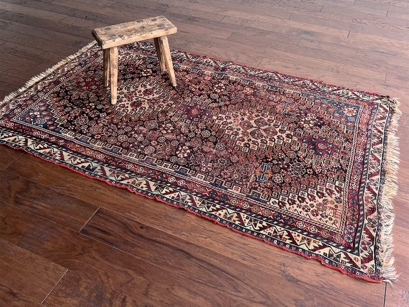 an antique shiraz rug with rust, brown and blue hues with an intricate floral pattern