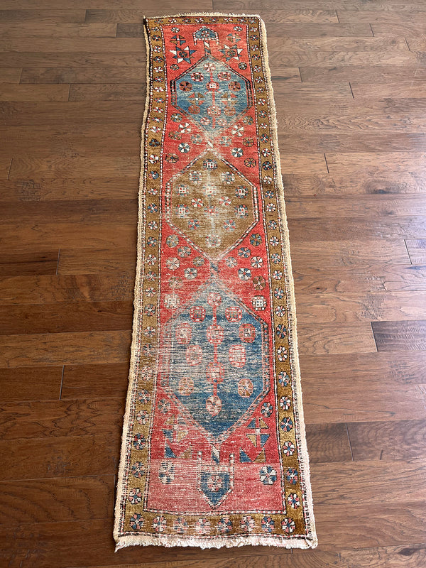 an antique heriz runner with a red and coral toned field and blue medallions