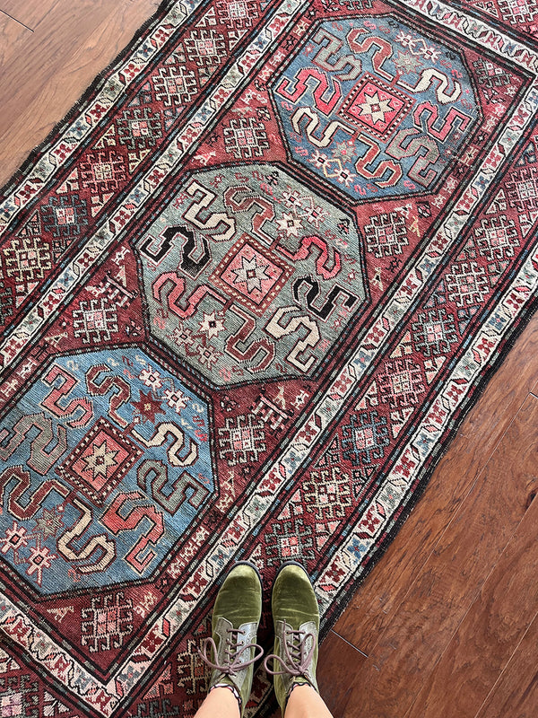 an antique caucasian kazak rug with a brick red palette and bright blue and green medallions