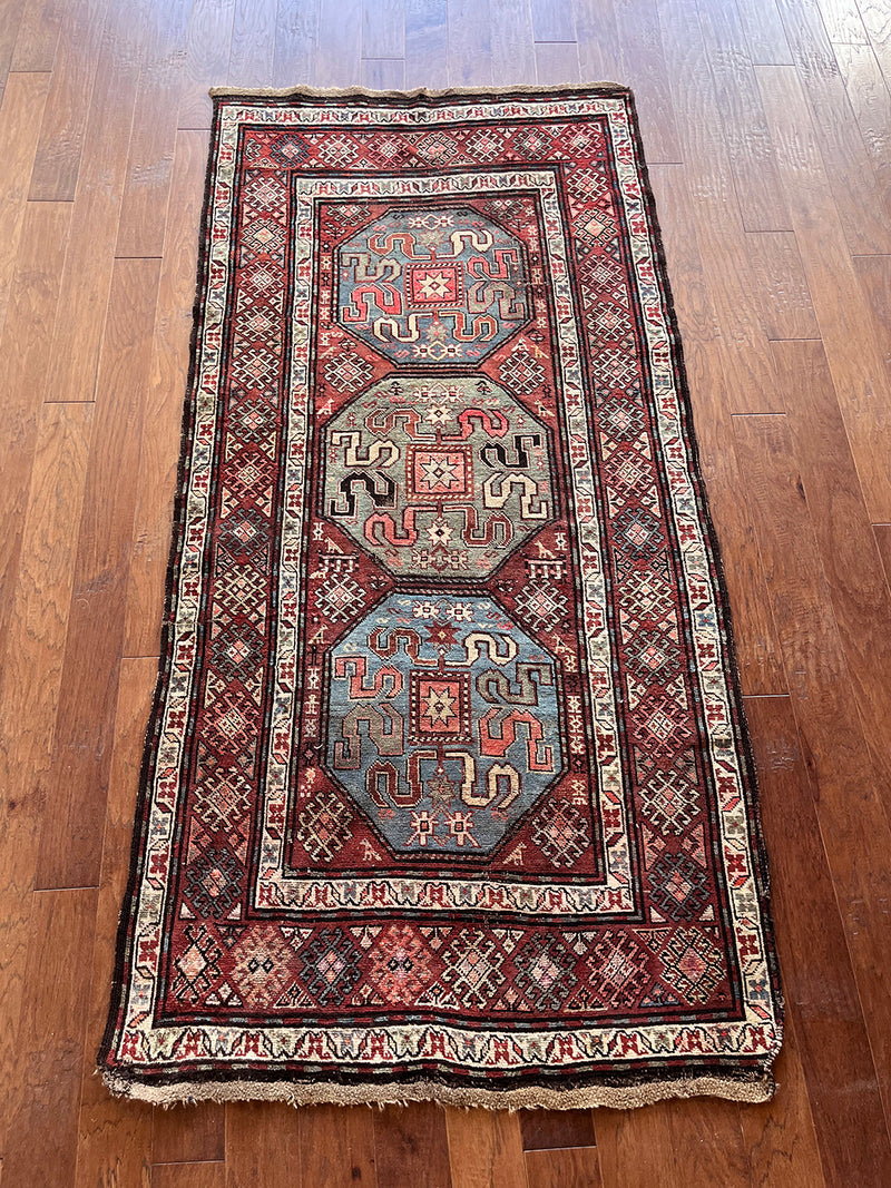an antique caucasian kazak rug with a brick red palette and bright blue and green medallions