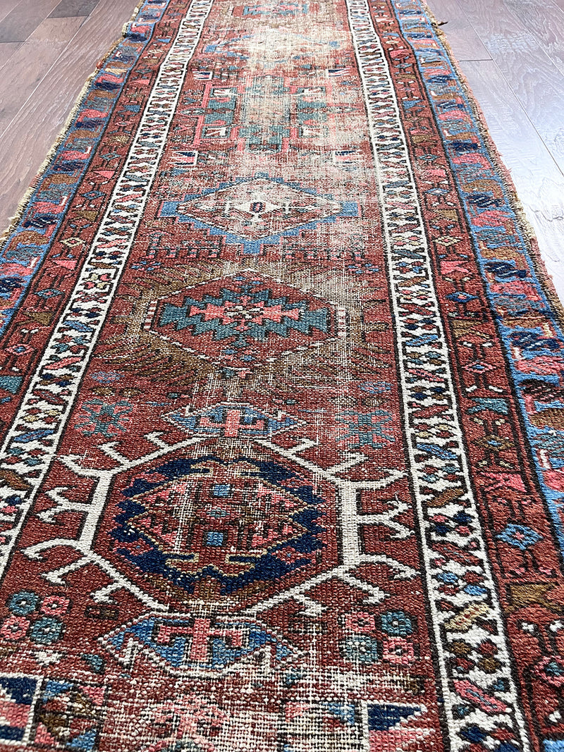 an antique heriz karajah runner with a brick red field with green and blue medallions