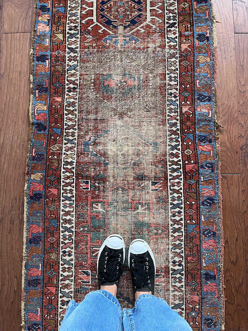 an antique heriz karajah runner with a brick red field with green and blue medallions