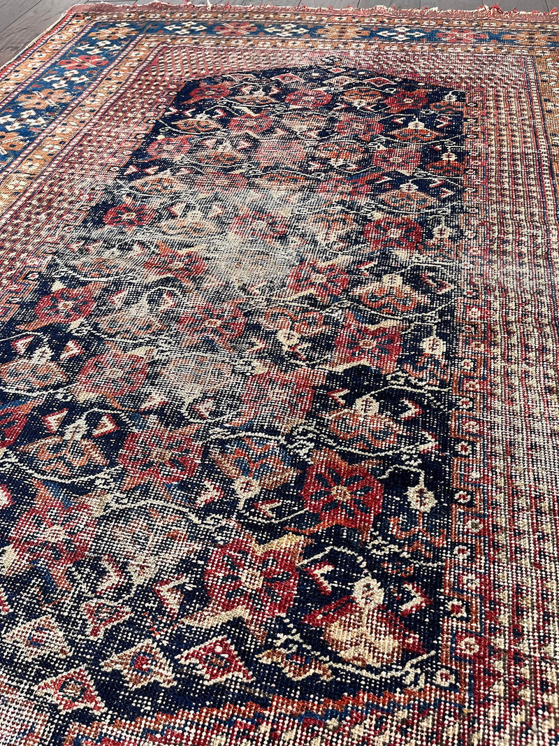 an antique afshar rug with a midnight blue medallion, intricate floral pattern and dot details 