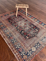 an antique afshar rug with a midnight blue medallion, intricate floral pattern and dot details 