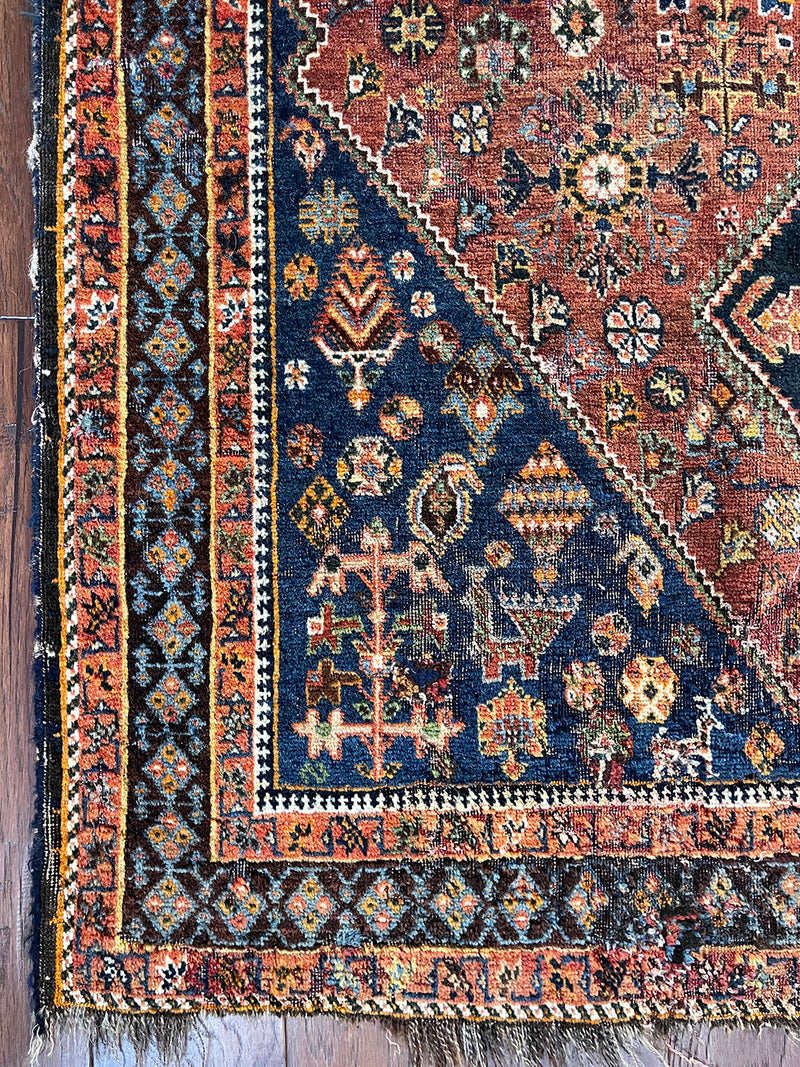 an antique qashqai rug with a dark terracotta field and blue and cream medallions