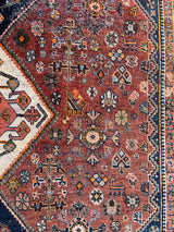 an antique qashqai rug with a dark terracotta field and blue and cream medallions