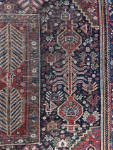 an antique qashqai rug with a dark field and tree of life pattern in brick red 