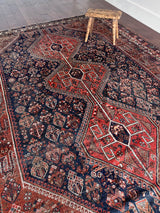 a large antique qashqai rug with a dark blue field and red central medallions