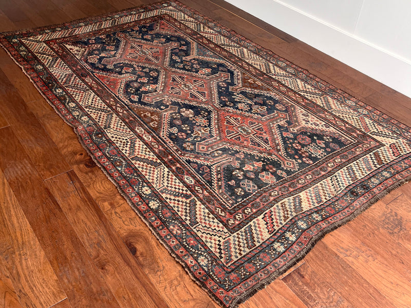 an antique qashqai rug with a dark blue field and brick red central medallions