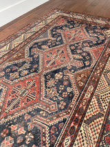 an antique qashqai rug with a dark blue field and brick red central medallions