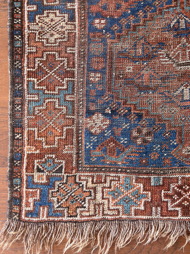 a mini antique qashqai rug with a dark blue field and brick red central medallions