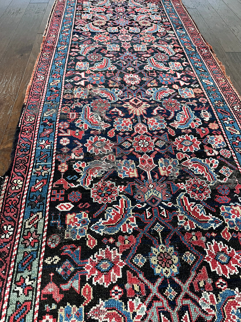 am antique heriz runner with a near black field and a pink and blue floral pattern