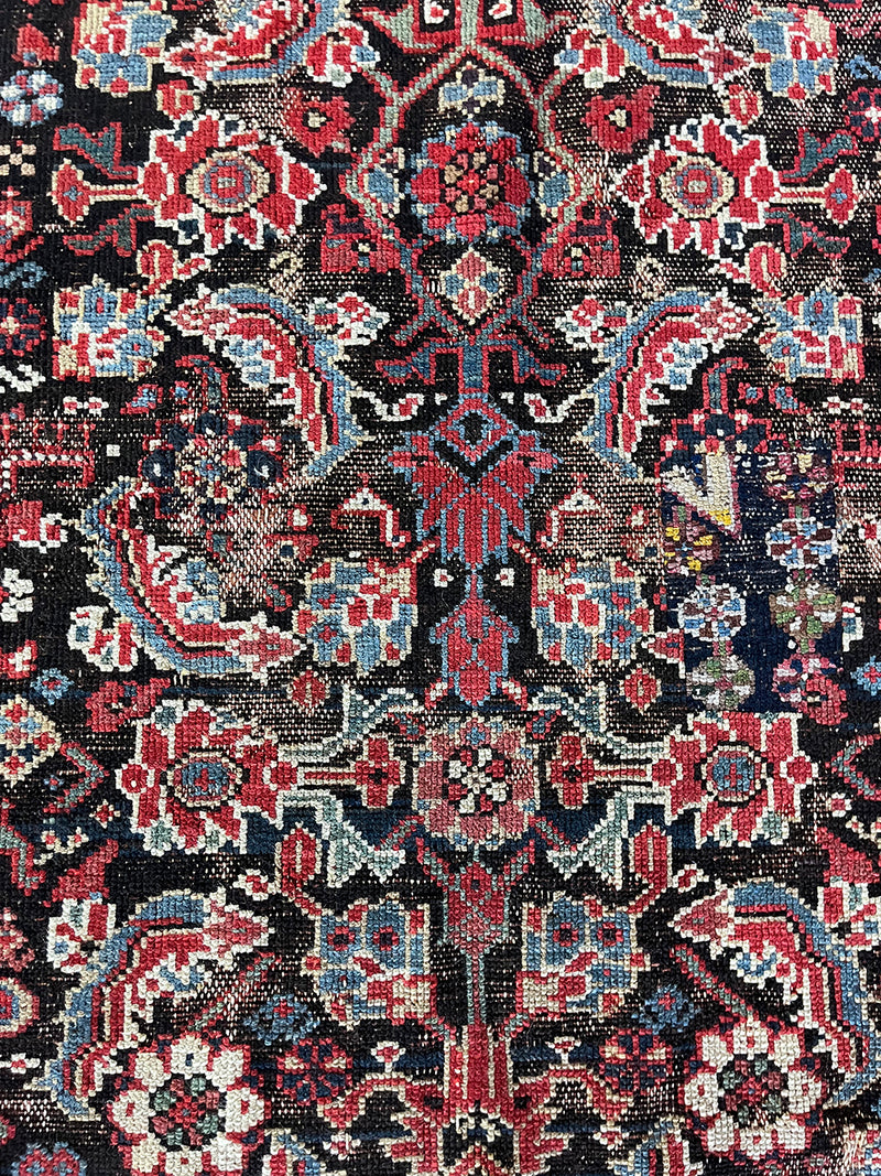 am antique heriz runner with a near black field and a pink and blue floral pattern
