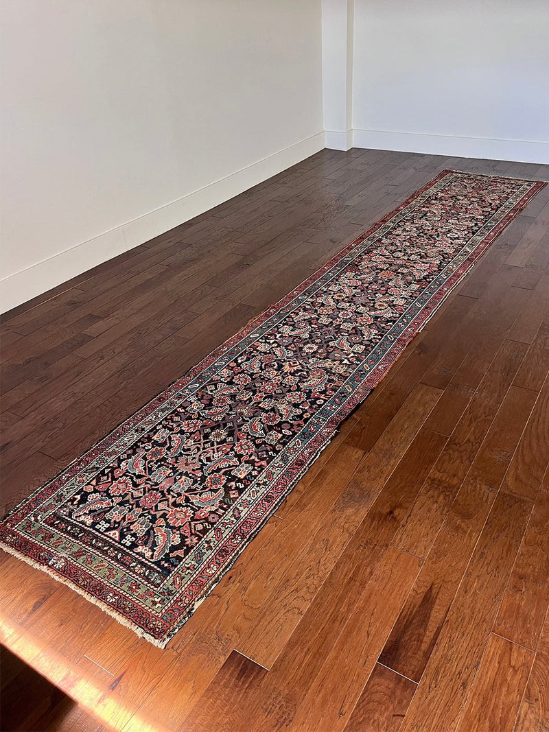 am antique heriz runner with a near black field and a pink and blue floral pattern