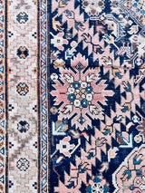 an antique caucasian rug with a dark blue field, cream border and soft pink details