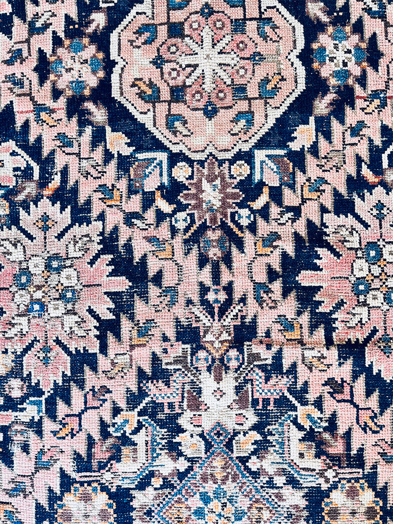 an antique caucasian rug with a dark blue field, cream border and soft pink details