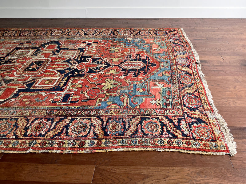 a large antique heriz rug with pink, coral, blue and green accents and a large navy blue medallion