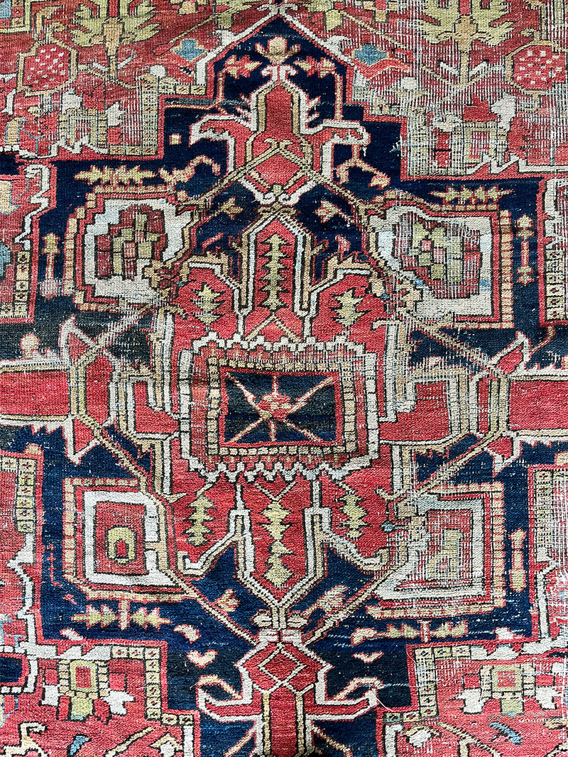 a large antique heriz rug with pink, coral, blue and green accents and a large navy blue medallion