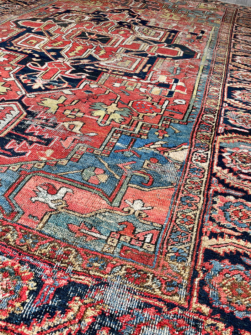a large antique heriz rug with pink, coral, blue and green accents and a large navy blue medallion