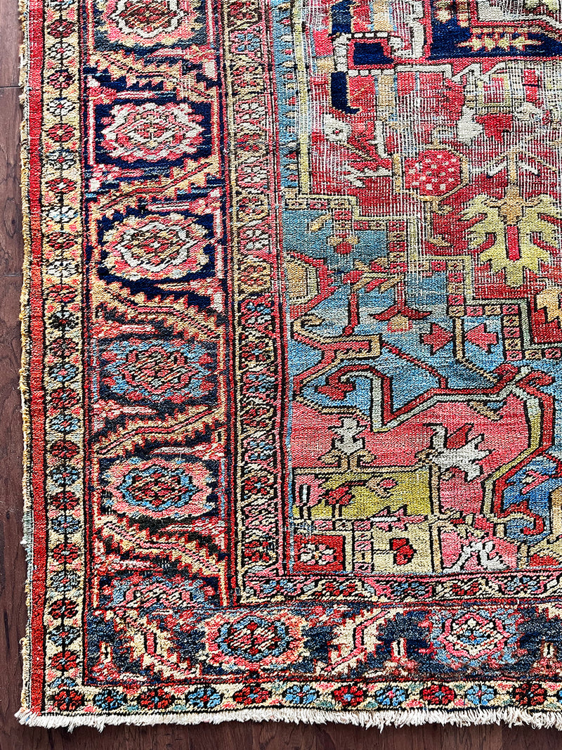 a large antique heriz rug with pink, coral, blue and green accents and a large navy blue medallion