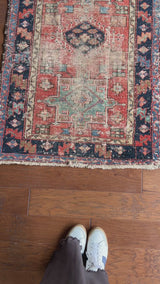 a pair of antique heriz karajah rugs in a faded salmon pink colour with teal and dark blue accents