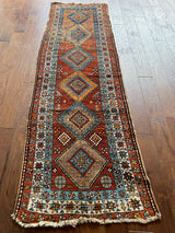 a vintage heriz runner with a rusty brown field and teal and taupe central medallions with a white border and star motifs