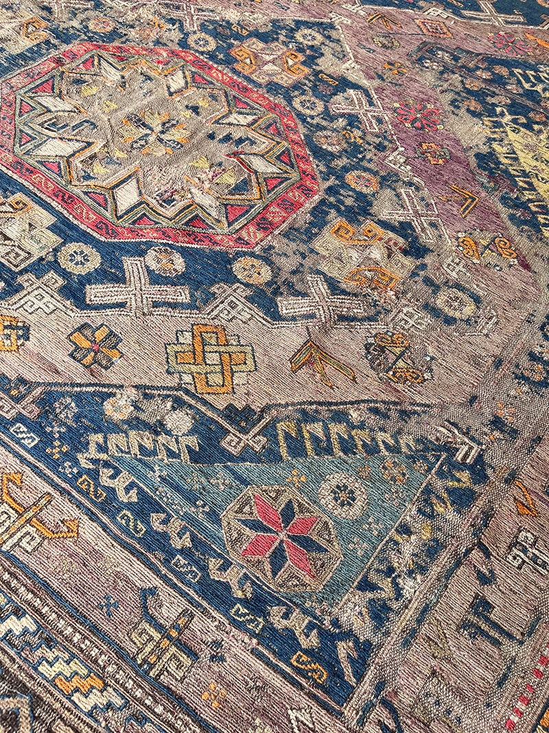 a large antique sumac rug with a purple field. blue medallions and hot pink accents