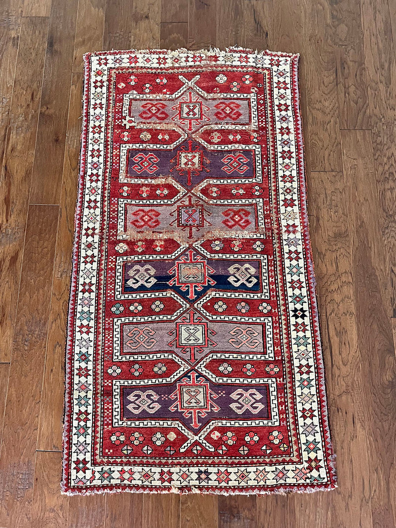 an antique caucasian rug with a red field and medallions in lilac and dark purple