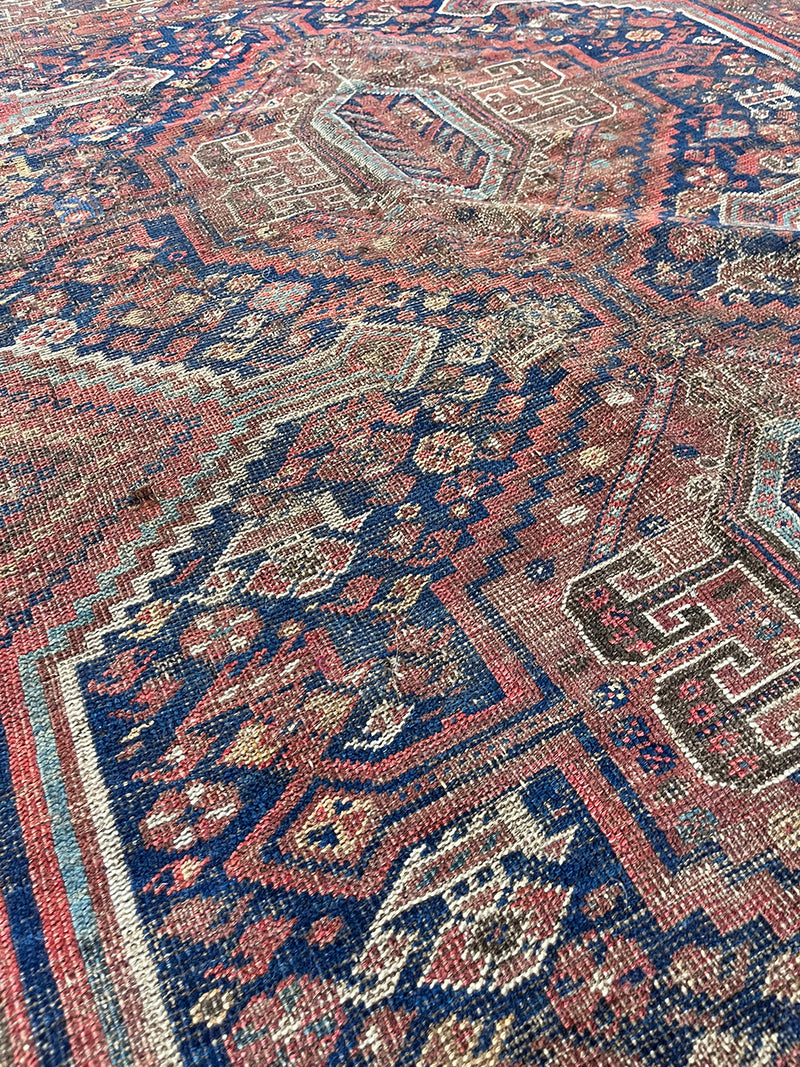 an antique qashqai rug with a dark blue field and warm brown details