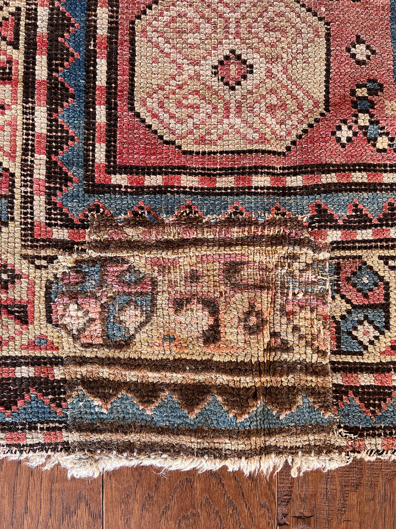 an antique caucasian rug with a red field and a blue and green geometric design