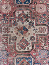an antique caucasian rug with a red field and a blue and green geometric design