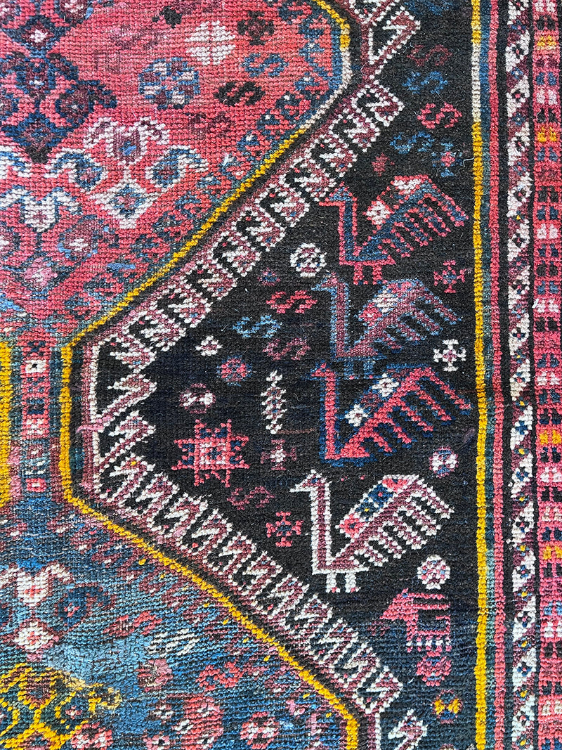 a vintage qashqai rug with a dark blue field and hot pink and yellow accents