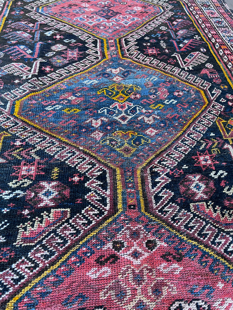 a vintage qashqai rug with a dark blue field and hot pink and yellow accents