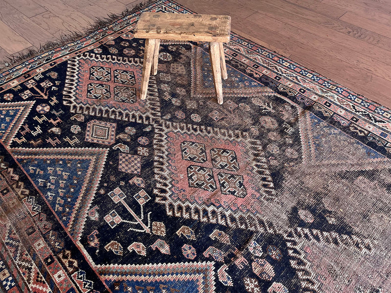 a medium antique qashqai rug with a midnight blue field and a large coral medallion