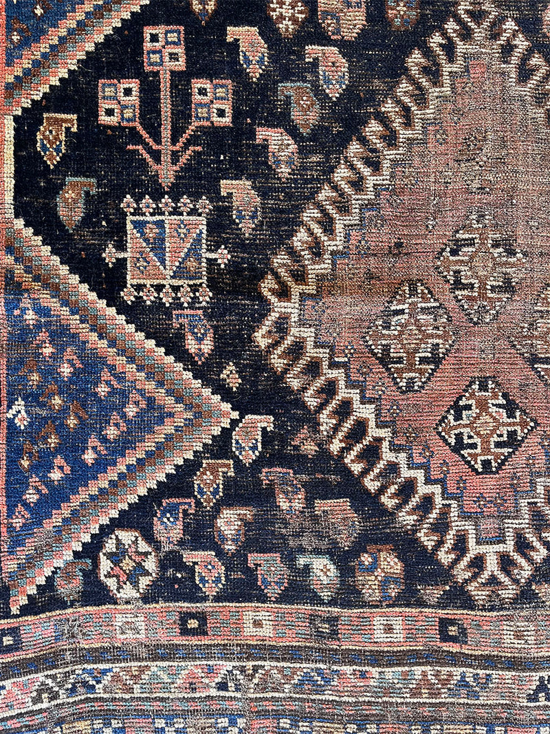 a medium antique qashqai rug with a midnight blue field and a large coral medallion