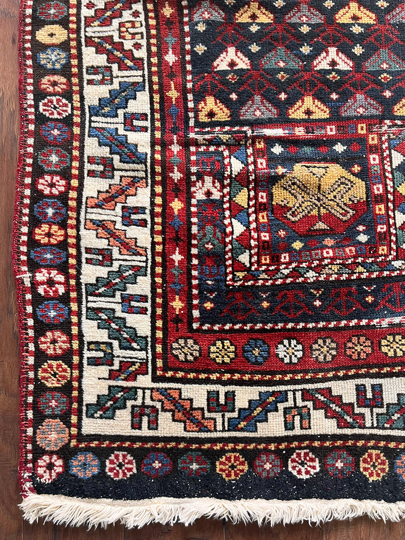 an antique caucasian prayer rug with a midnight blue field and colourful accents